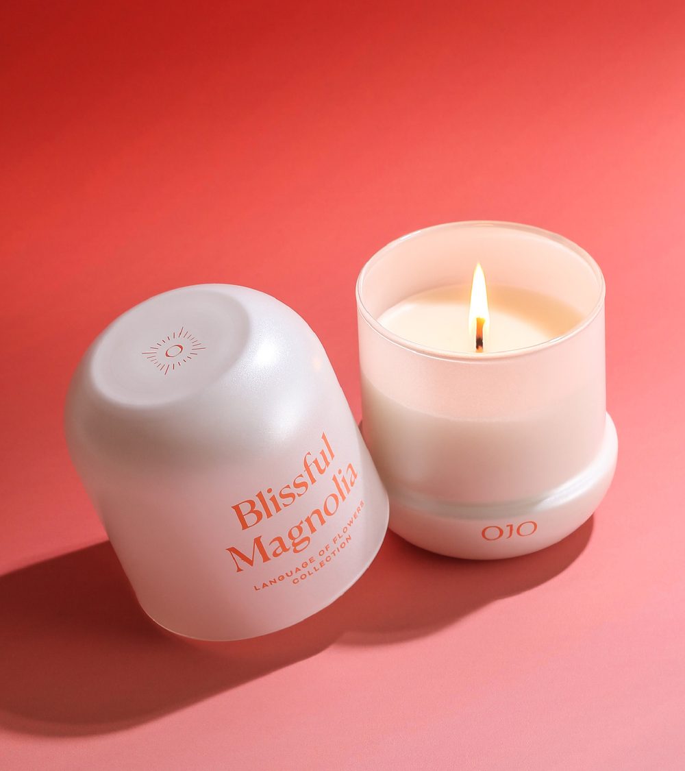 OJO Blissful Magnolia candle with white glass jar and orange pink background