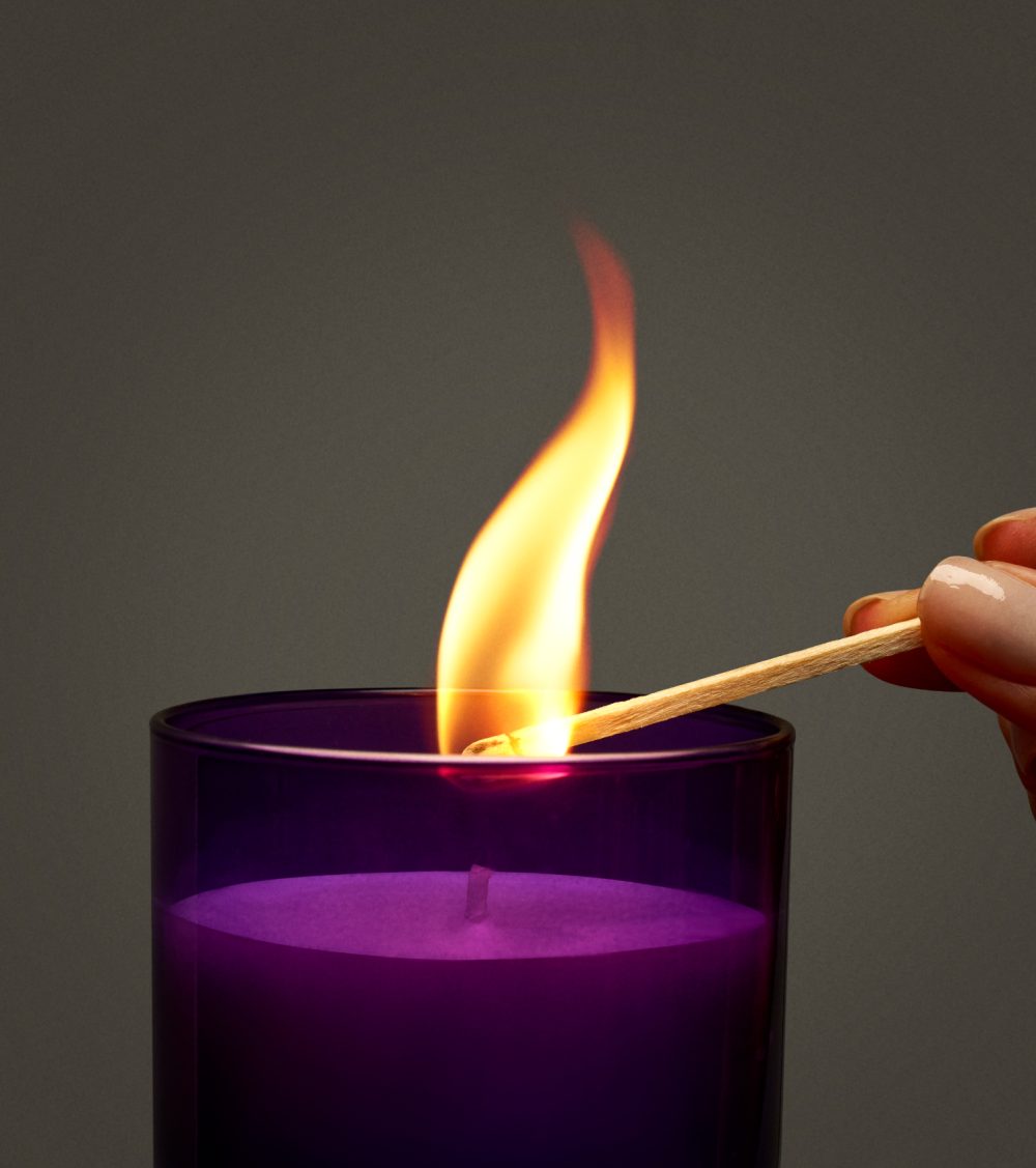 OJO candle, purple glass jar, burning candle with matches and gray background