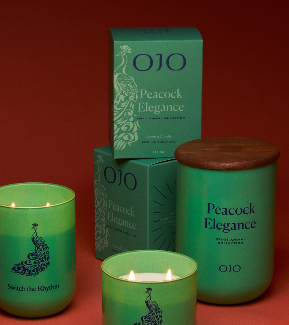OJO Peacock Elegance candle collection with green, turquoise glass jar, turquoise packaging box and orange background