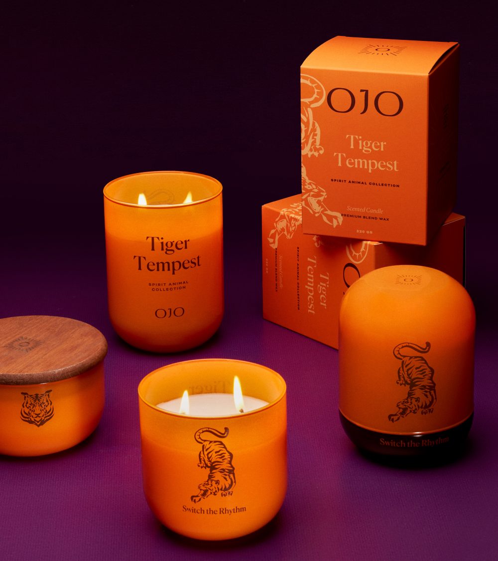 OJO Tiger Tempest candle collection with orange glass jars, orange packaging box and purple background
