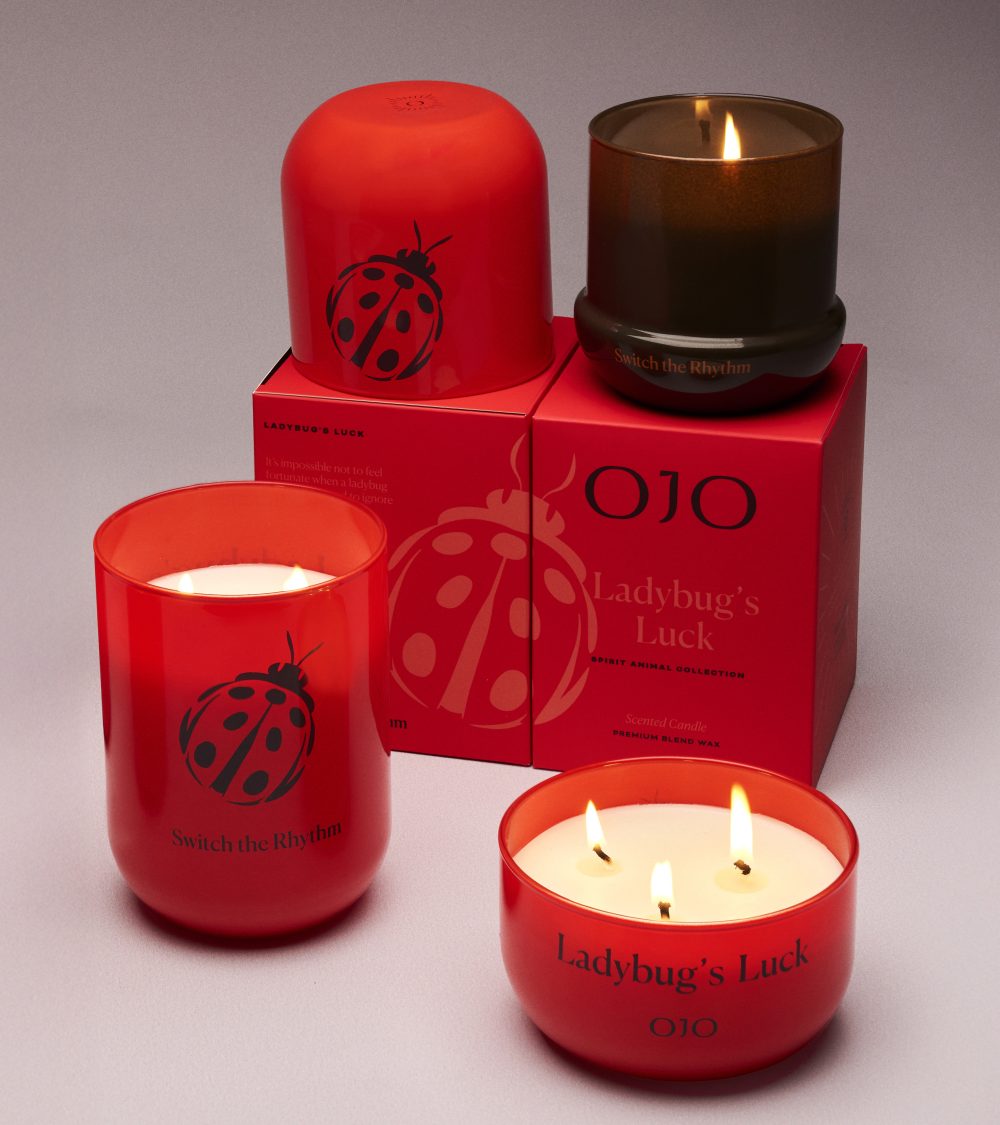 OJO Ladybug's Luck candle collection with red and black glass jar, red packaging box and gray background